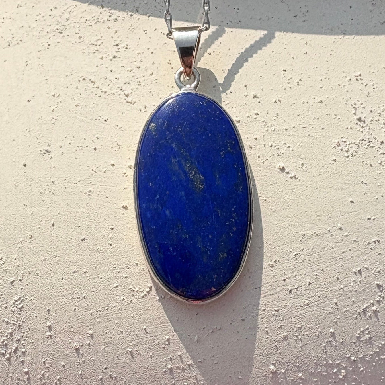 A silver pendant necklace with an oval blue stone is draped over a large white ceramic jug outdoors.