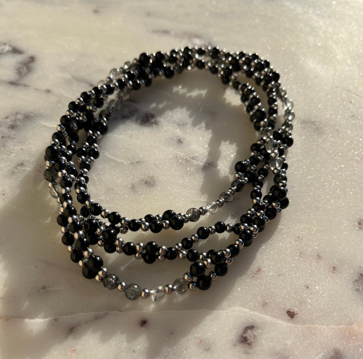 Three beaded stretch bracelets in black and silver, arranged in a circle on a white marble surface.