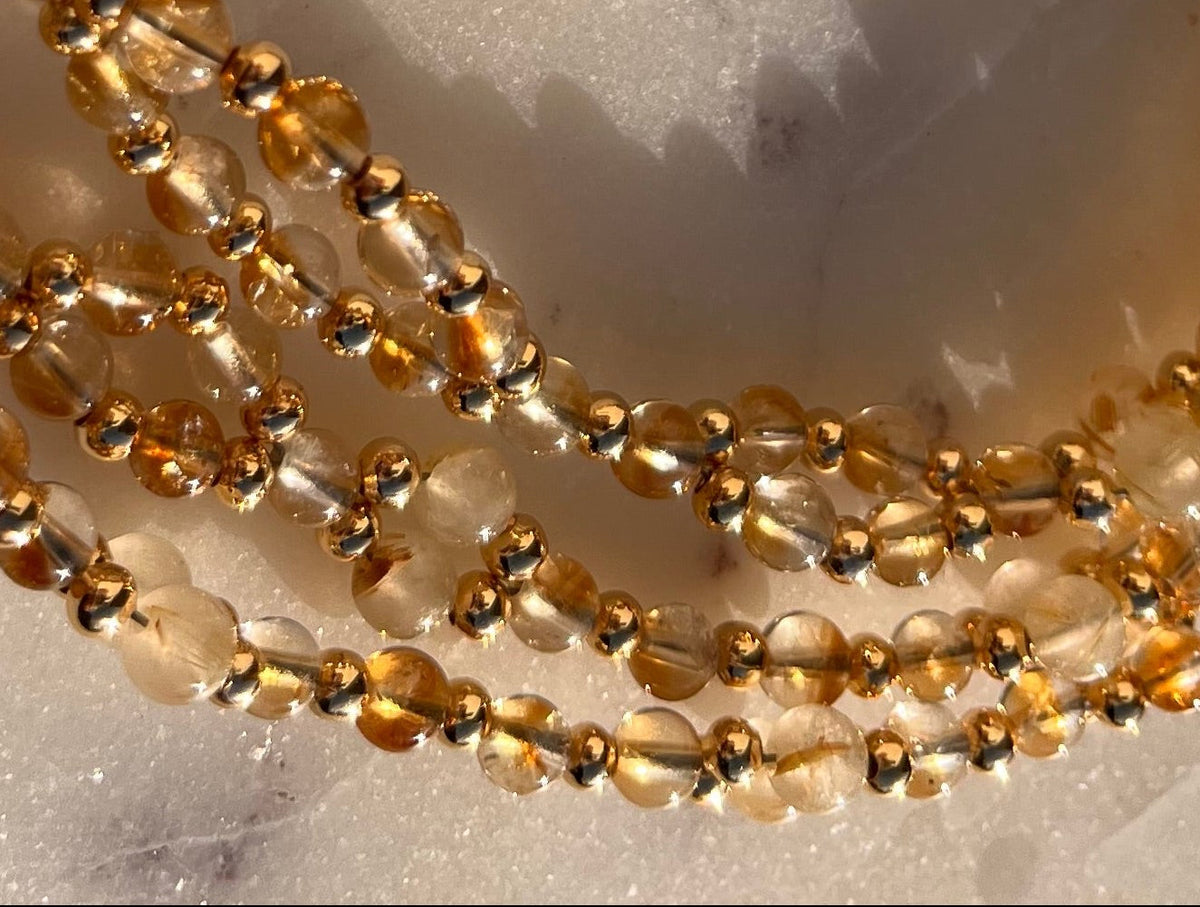 A coiled strand of small amber-brown translucent beads, likely a beaded necklace or bracelet, photographed on a light marble surface with visible dark veining.