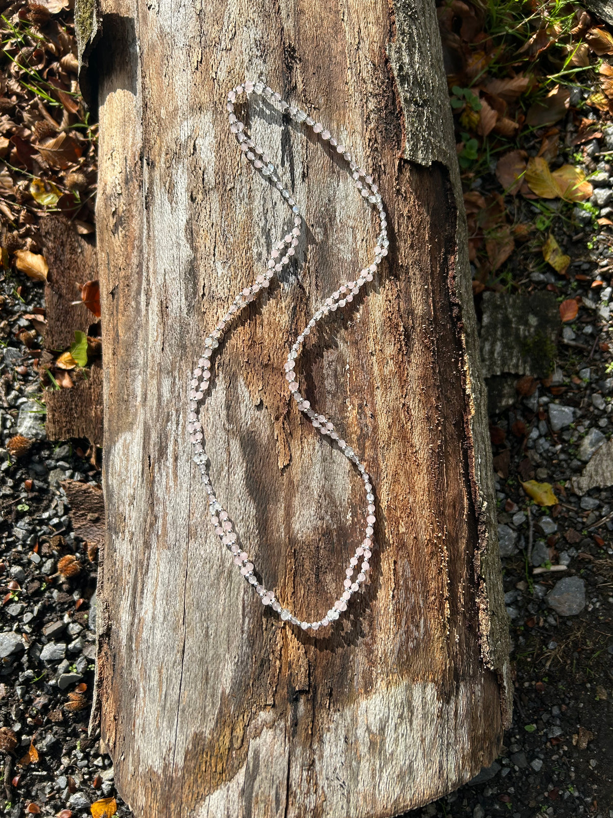 A beaded necklace made of light pink faceted beads separated by small metallic silver spacer beads, laid out on a beige marble surface.