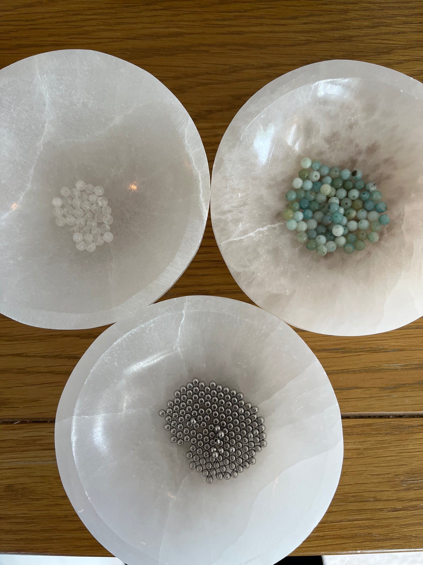 Amazonite and Rainbow Moonstone beads resting in a carved selenite bowl before being handcrafted into a sacred geometric tantric necklace, photographed in natural light.