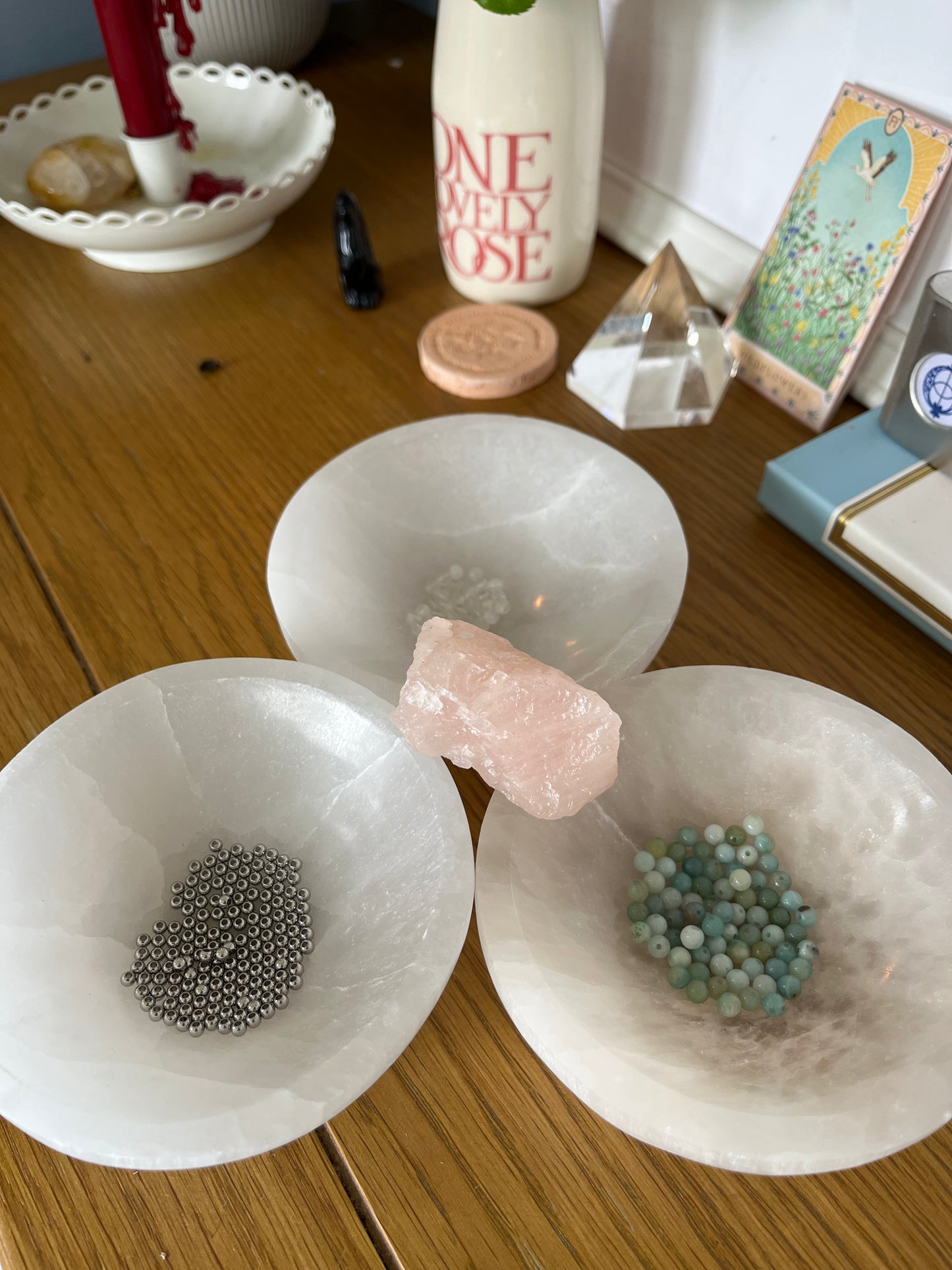 Amazonite and Rainbow Moonstone beads resting in a carved selenite bowl before being handcrafted into a sacred geometric tantric necklace, photographed in natural light.