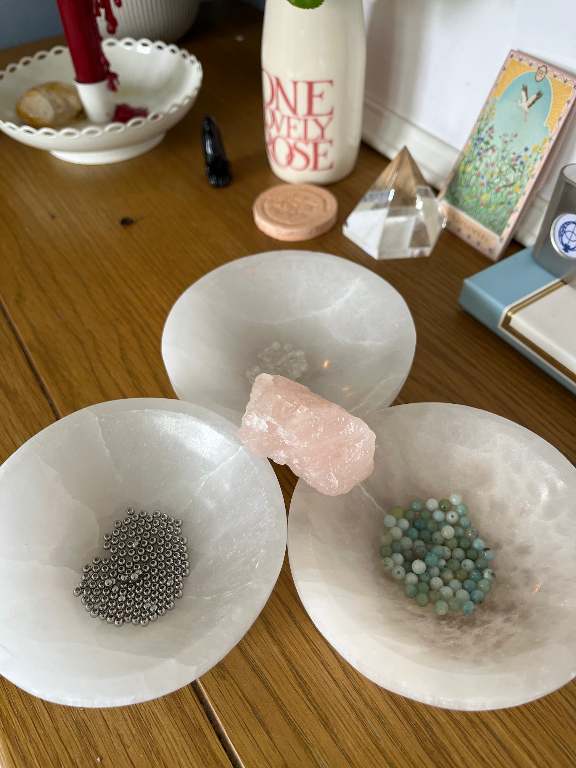Amazonite and Rainbow Moonstone beads resting in a carved selenite bowl before being handcrafted into a sacred geometric tantric necklace, photographed in natural light.